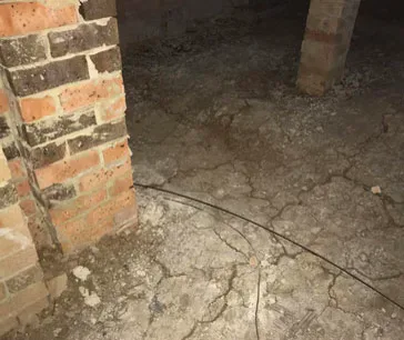 Brick piers under a house standing on cracked, dried-out soil