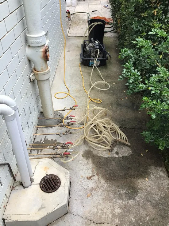 DampBlock injection equipment and hoses connected to base of Ashgrove unit building wall