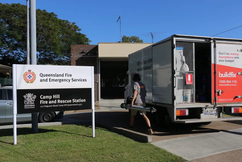 Queensland Fire and Emergency Services sign at Camp Hill Fire and Rescue Station with a Buildfix technician carrying a laser tripod to the driveway