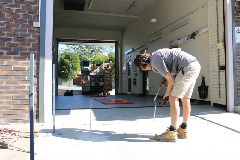 Buildfix technician drilling injection ports into the Camp Hill Fire Station driveway slab with a fire truck in the bay behind