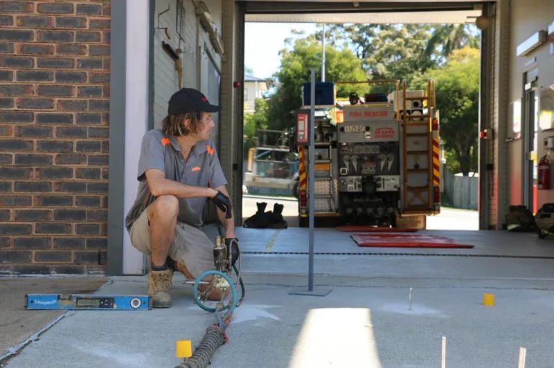 Buildfix technician injecting GeoPoly™ resin beneath the Camp Hill Fire Station driveway with a laser level set up and a fire truck behind