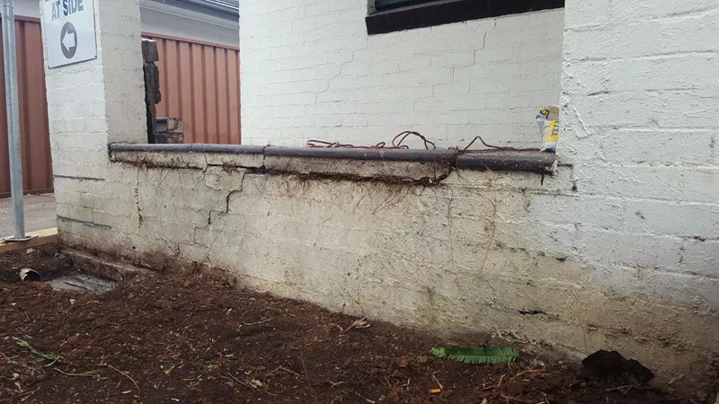 Side wall of the Summer Hill surgery verandah with a wide crack through the painted brick and bare eroded soil where rainwater had pooled against the footing