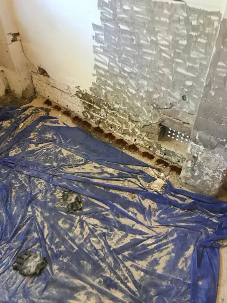 Stripped plaster revealing damaged brick and injection holes at base of Frenchs Forest wall