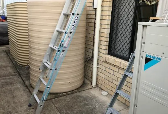 The 10,000-litre rainwater tank beside the brick extension, with the overflow pipe that was never connected