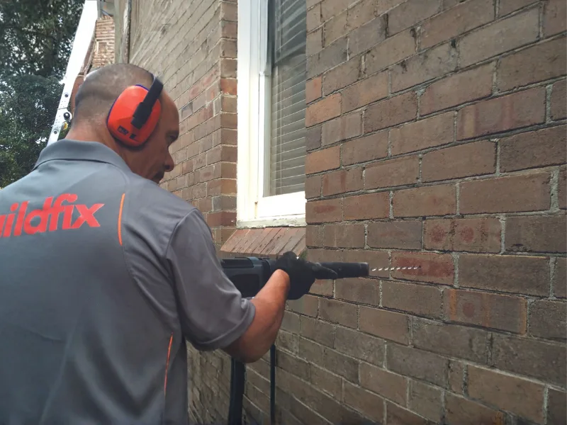 Buildfix technician drilling HelicalBar R304 stainless steel wall ties into coastal brick wall