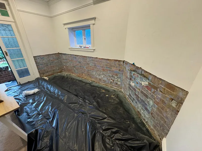 Exposed damaged brick wall with plaster stripped back revealing rising damp damage at Mosman home