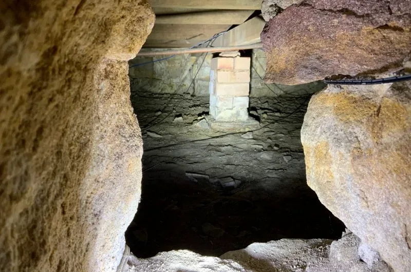 Subfloor under the Mosman house seen through the sandstone footing, a brick pier standing on eroded soil beneath the bearers