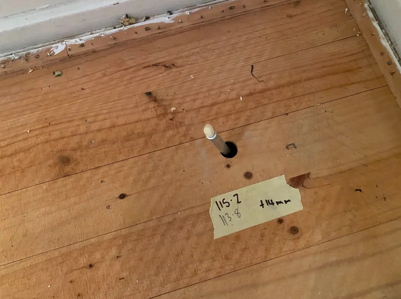 Injection hole in floorboard with measurement tape showing 14mm lift