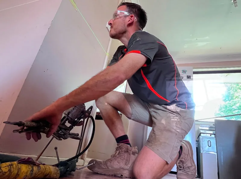 Buildfix technician kneeling with injection equipment on living room floor