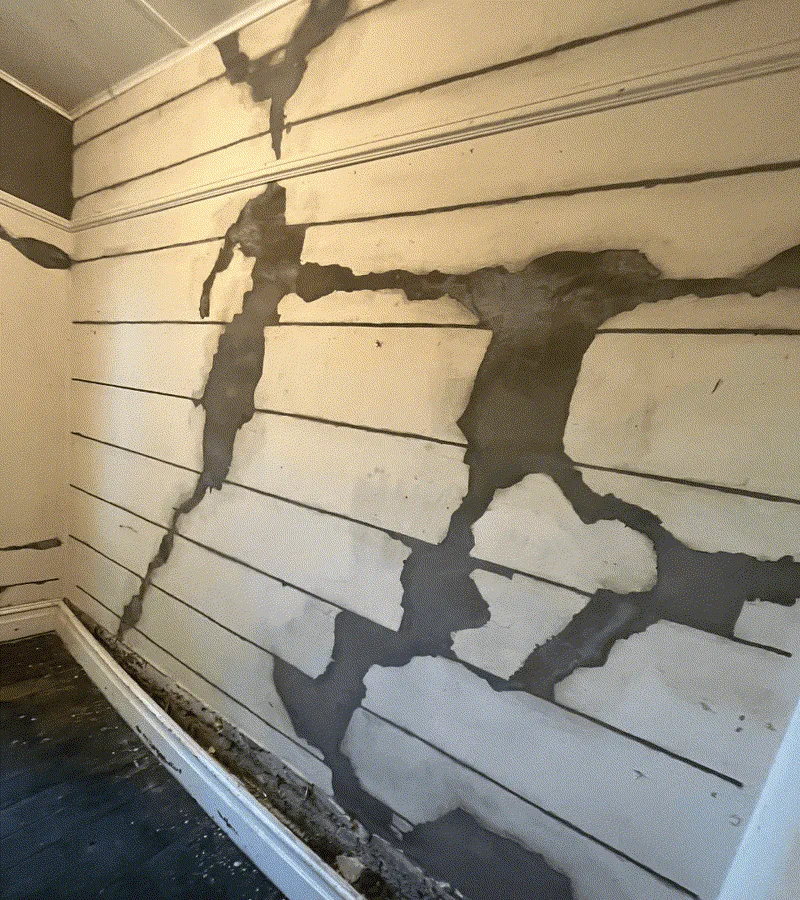 Cracked interior wall with large plaster patches exposing brickwork