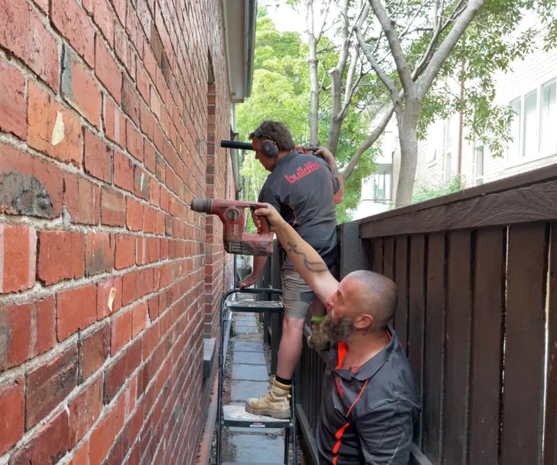 Buildfix technicians installing HelicalBar ties on external brick wall in narrow access