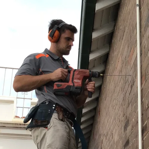 Buildfix technician drilling and installing stainless steel remedial wall ties into mortar joints