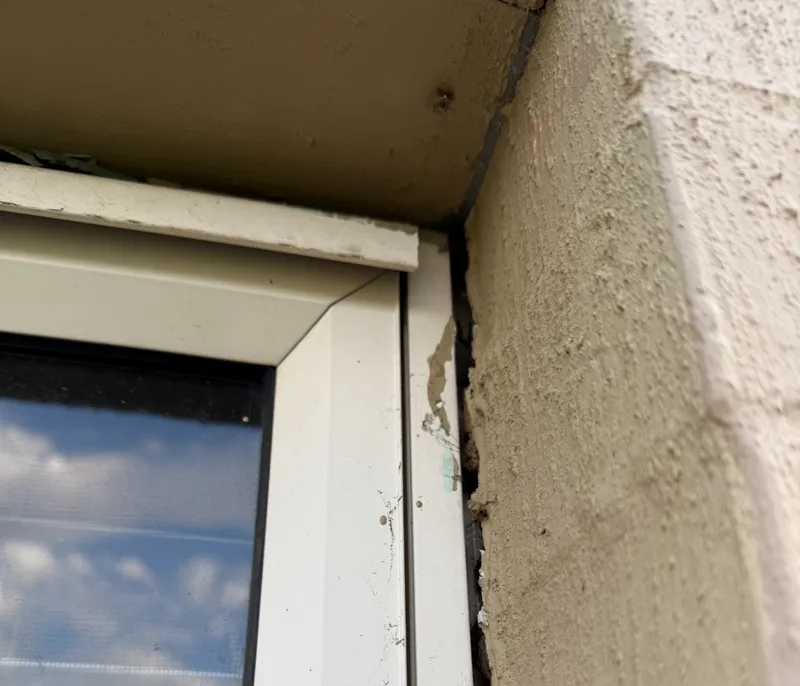 Gap between window frame and rendered wall with cracking paint and sealant from wall movement
