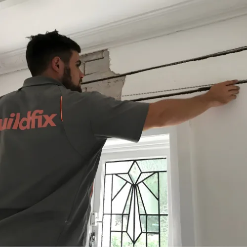 Buildfix technician installing stainless steel HelicalBars into mortar joints behind plaster wall