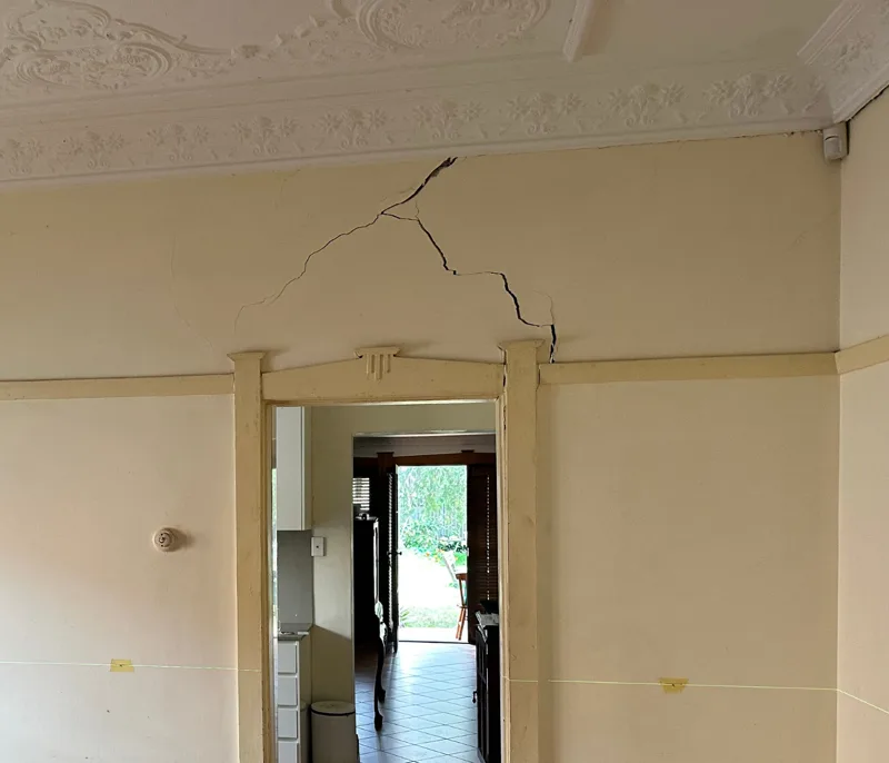 Plaster crack running diagonally above a door frame in an older home with ornate ceiling