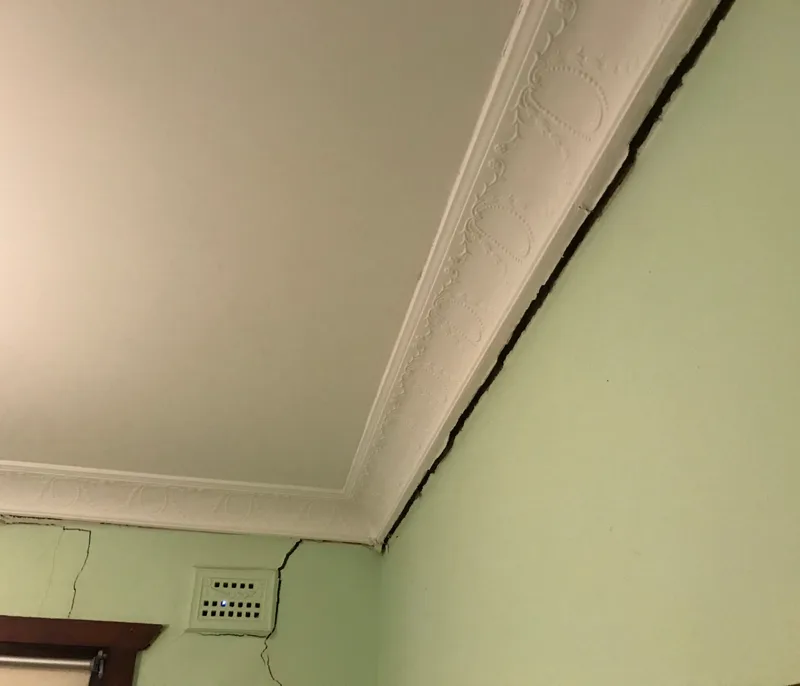 Dark gap between ceiling cornice and wall with visible plaster cracking below