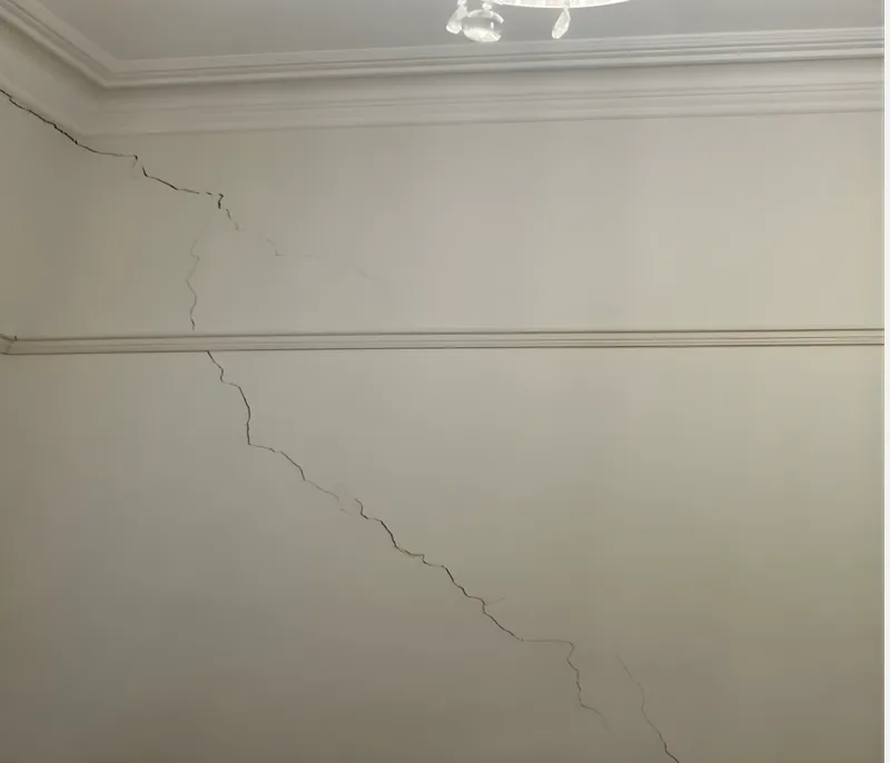 Long diagonal plaster crack running from near the floor to the ceiling cornice