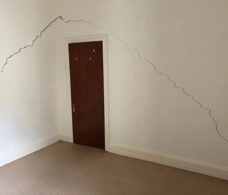 Wide branching plaster cracks spreading across an internal wall around a door frame