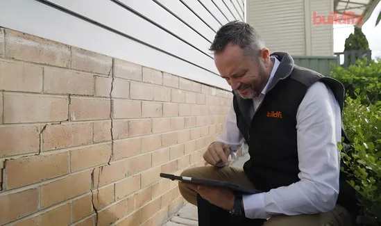 Buildfix structural engineer assessing cracked wall with tablet and laser level