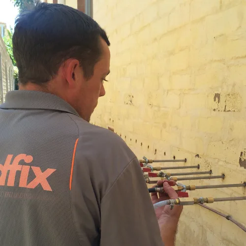 Buildfix technician injecting DampBlock resin into mortar course at base of brick wall