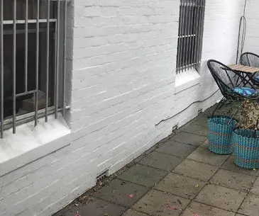 Rendered wall with large sections of render cracked, delaminated, and blown off exposing damaged masonry beneath