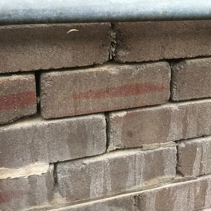External dark brickwork with white salt streaks running down through the mortar joints and across the face of the bricks