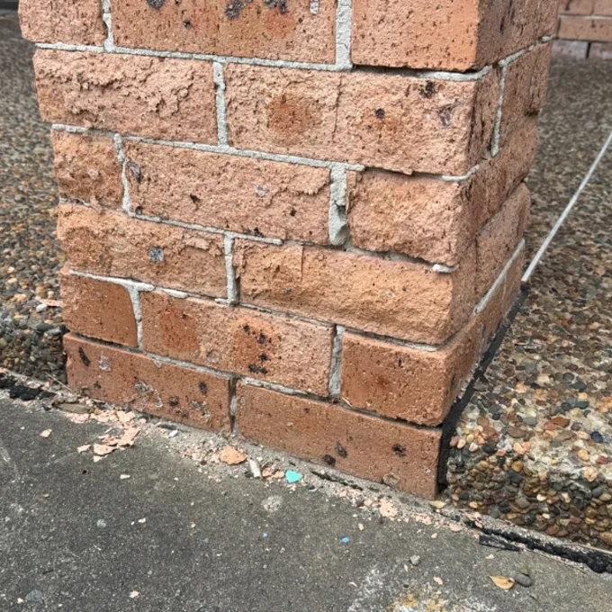 Brick pier at ground level with lower courses visibly darker and damp with mortar deterioration at the base