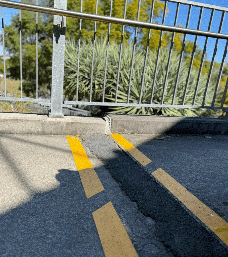 Sunken walkway with deep gap along yellow line markings near railing post
