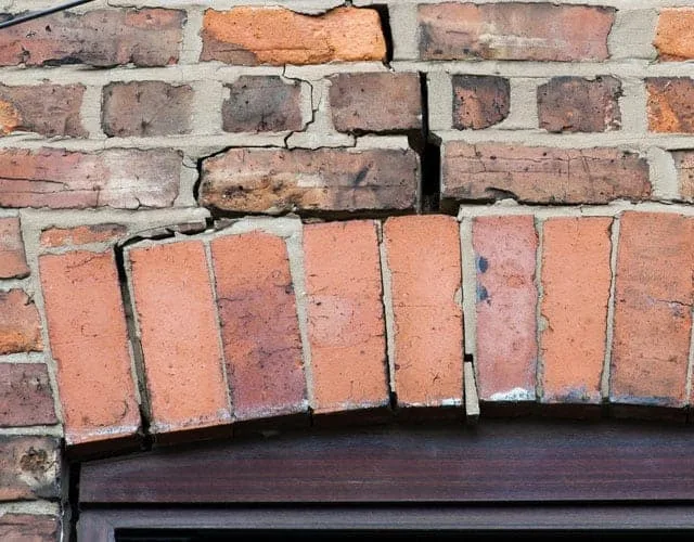Brick arch above a window broken and dropping as the wall beneath it subsides