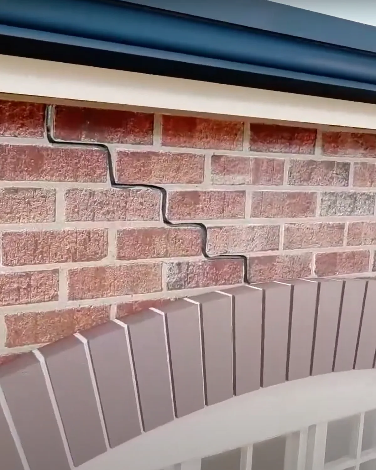 Stepped crack running up through the brickwork from a failed brick arch above a window