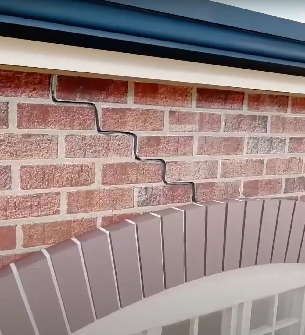 Stepped crack running up through the brickwork from a failed brick arch above a window