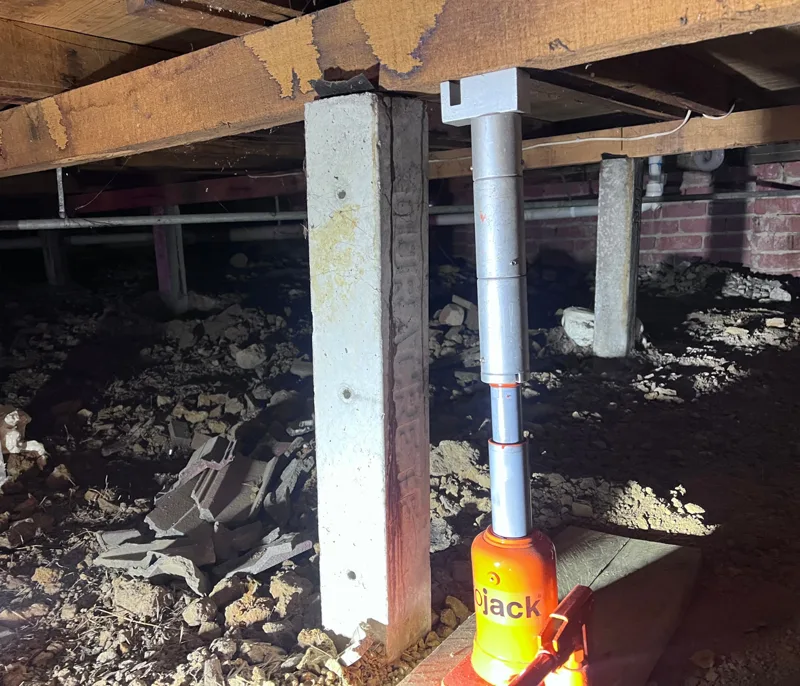 Hydraulic jack raising a timber bearer with wooden packers being fitted to brick pier