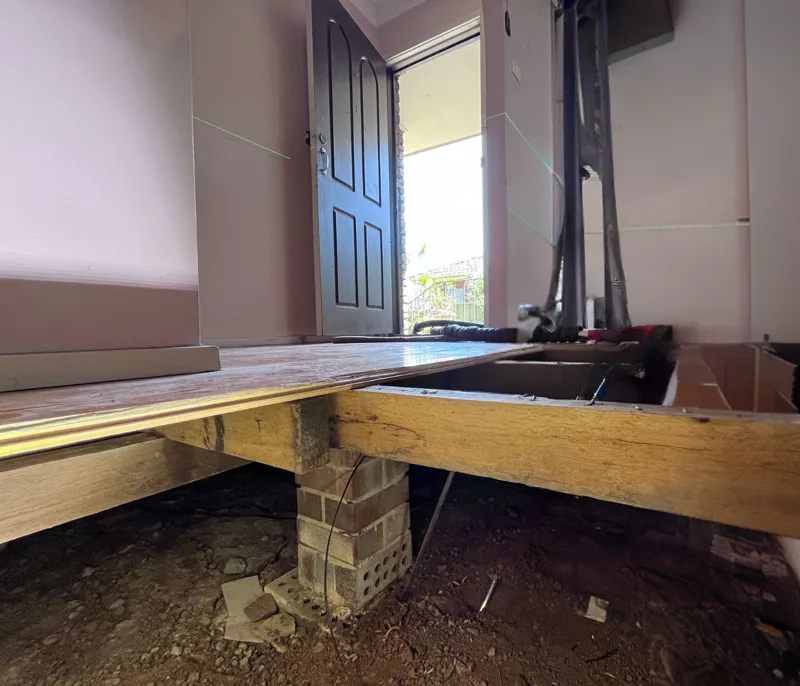 Floorboards lifted exposing bearer and brick stump beneath with subfloor visible