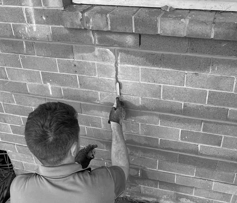 Tradesman repointing a stepped crack in a brick wall with a pointing tool