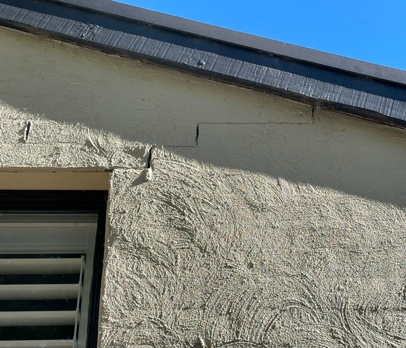 Minor diagonal crack in rendered wall near roofline caused by normal building settlement