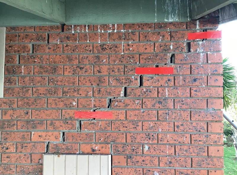 Staircase crack in brick wall with red tape markers