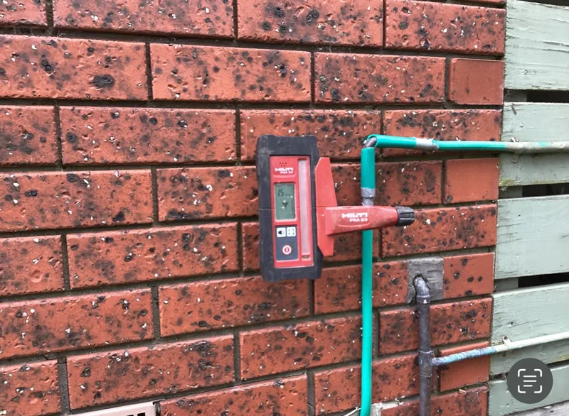 Laser level receiver on brick wall showing 15mm reading