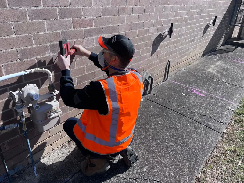 Worker in hi-vis using laser level on block wall at CSIRO