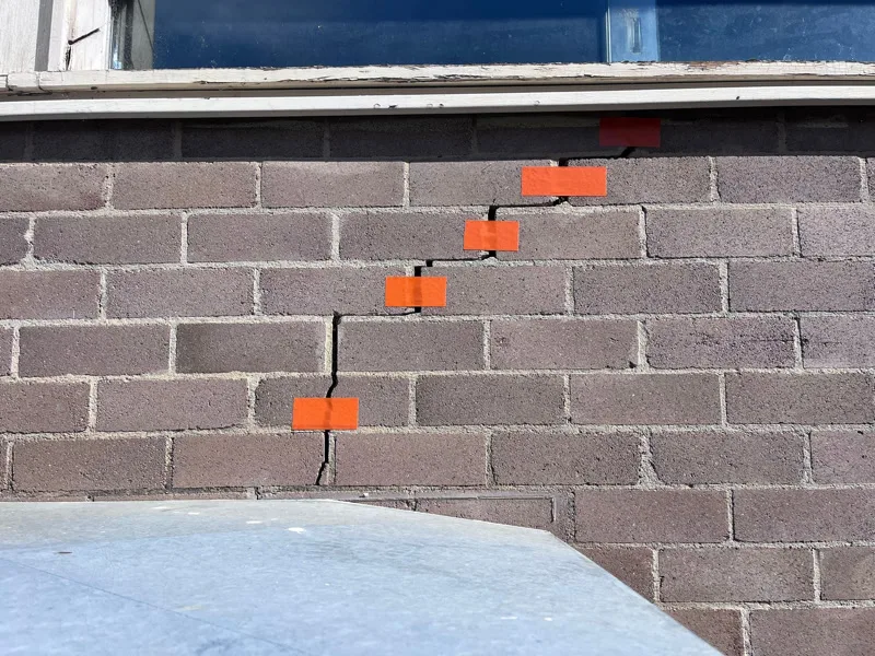 Staircase crack in block wall marked with orange tape