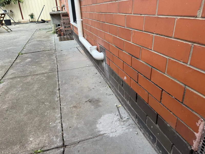 Brick wall base with downpipe showing foundation-level gap