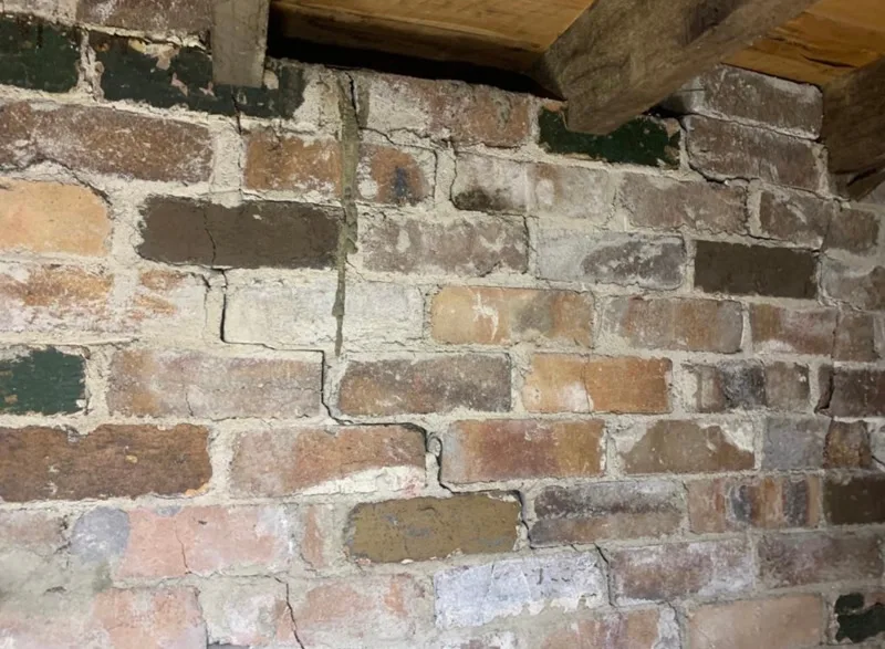 Vertical crack through old brick wall under timber beam