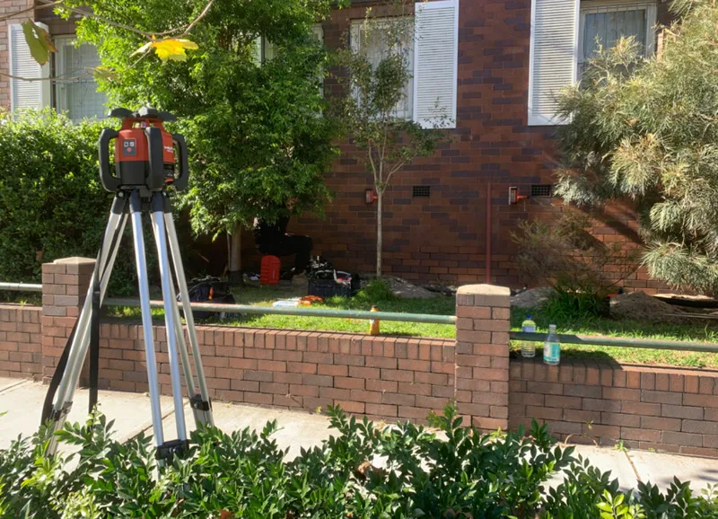 Laser level on tripod set up outside brick apartment building