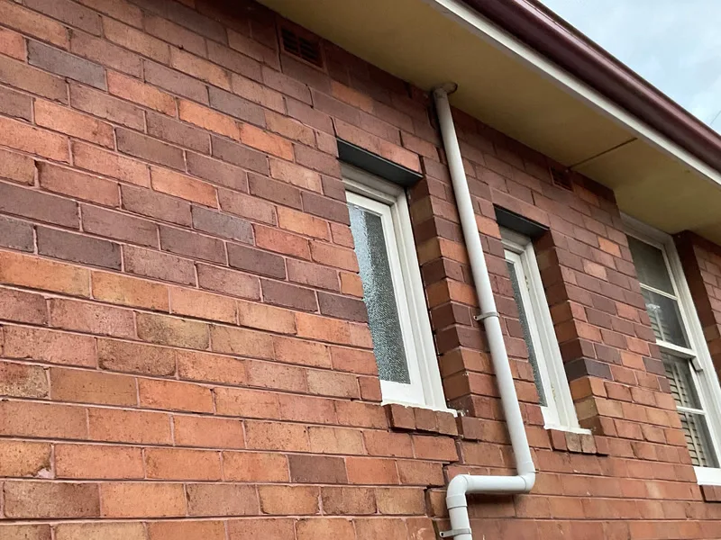 Brick wall with staircase crack near windows and downpipe