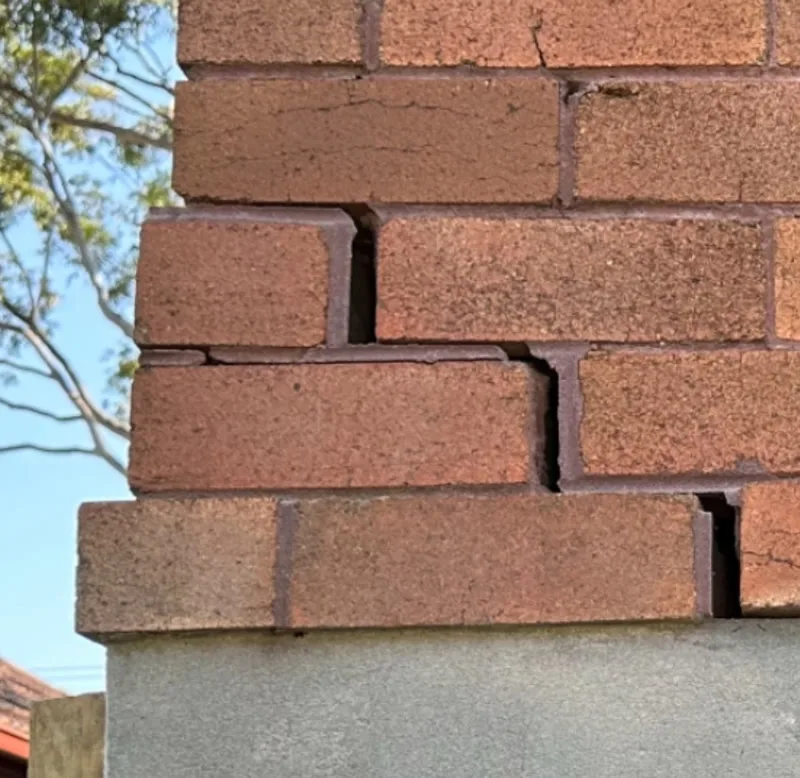 Severe staircase crack in brick corner above render wall