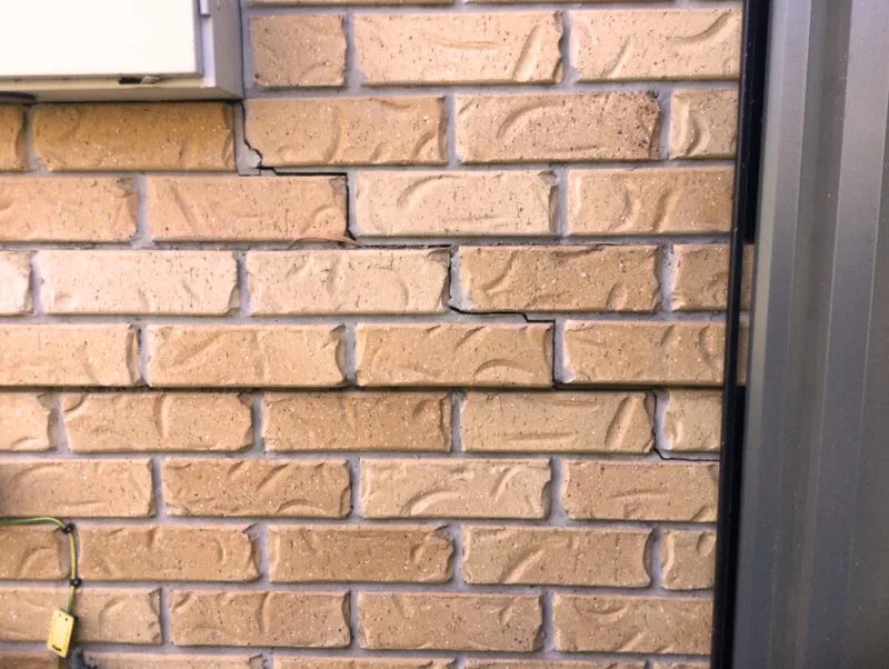 Staircase crack in buff brick wall near window and garage door