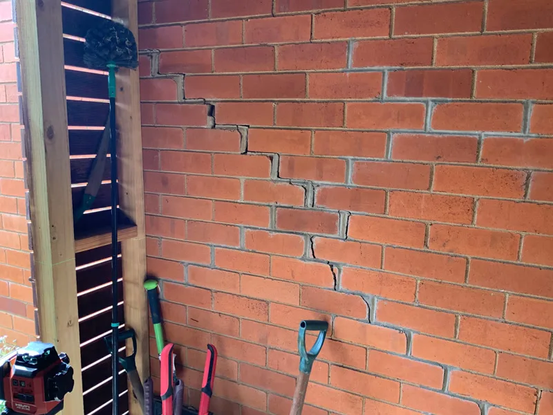 Large staircase crack in orange brick wall near garden tools
