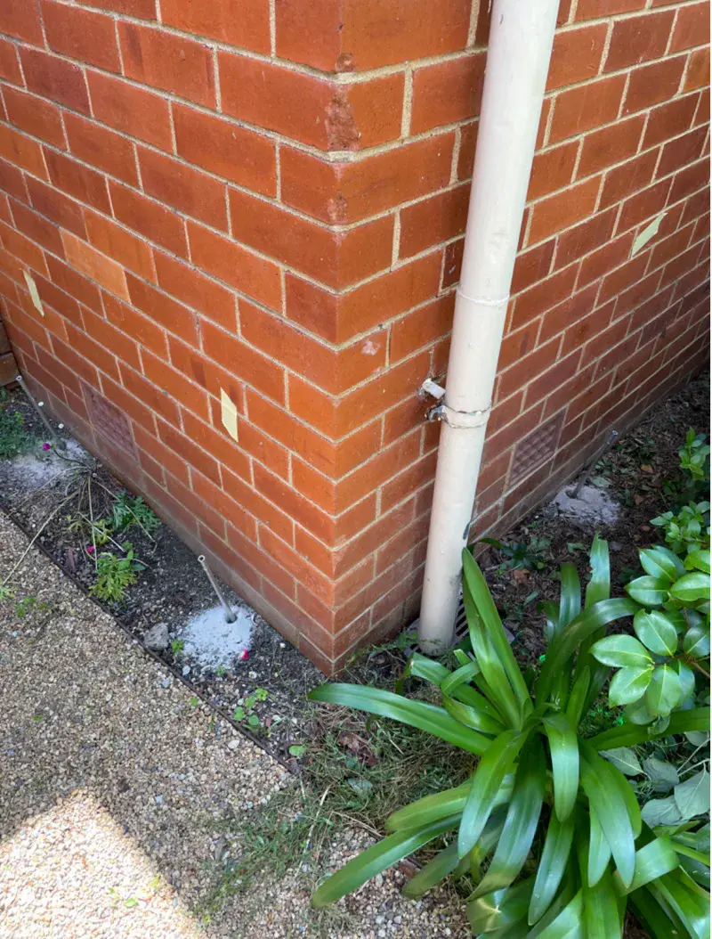 Brick wall corner with downpipe showing injection point markers