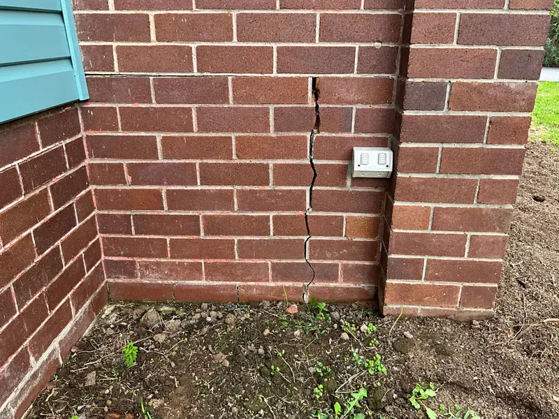 Vertical crack in brick wall corner near power outlet