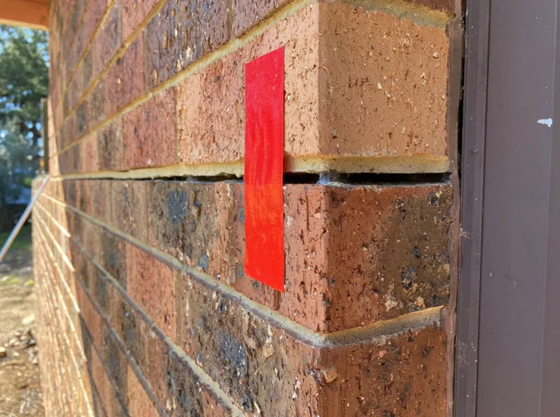 Red tape marking wide horizontal crack in brick corner