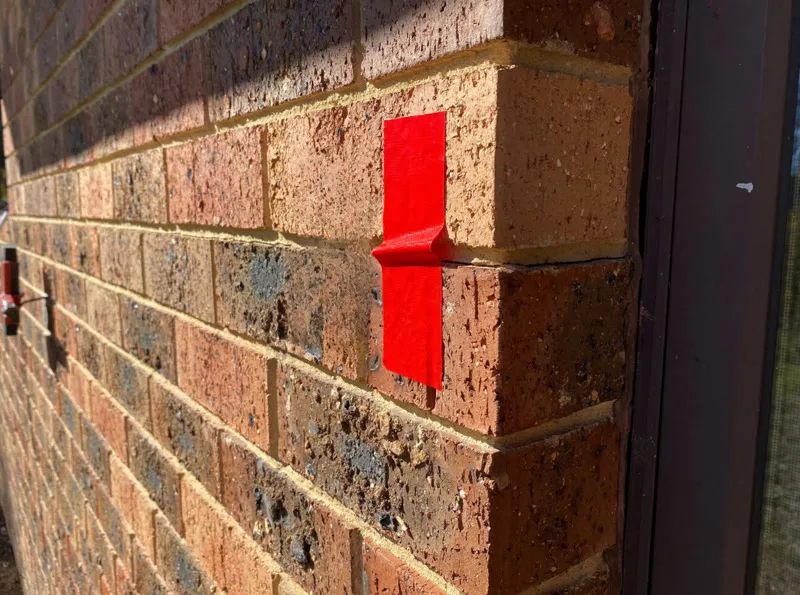 Red tape marking closed crack in brick wall after repair